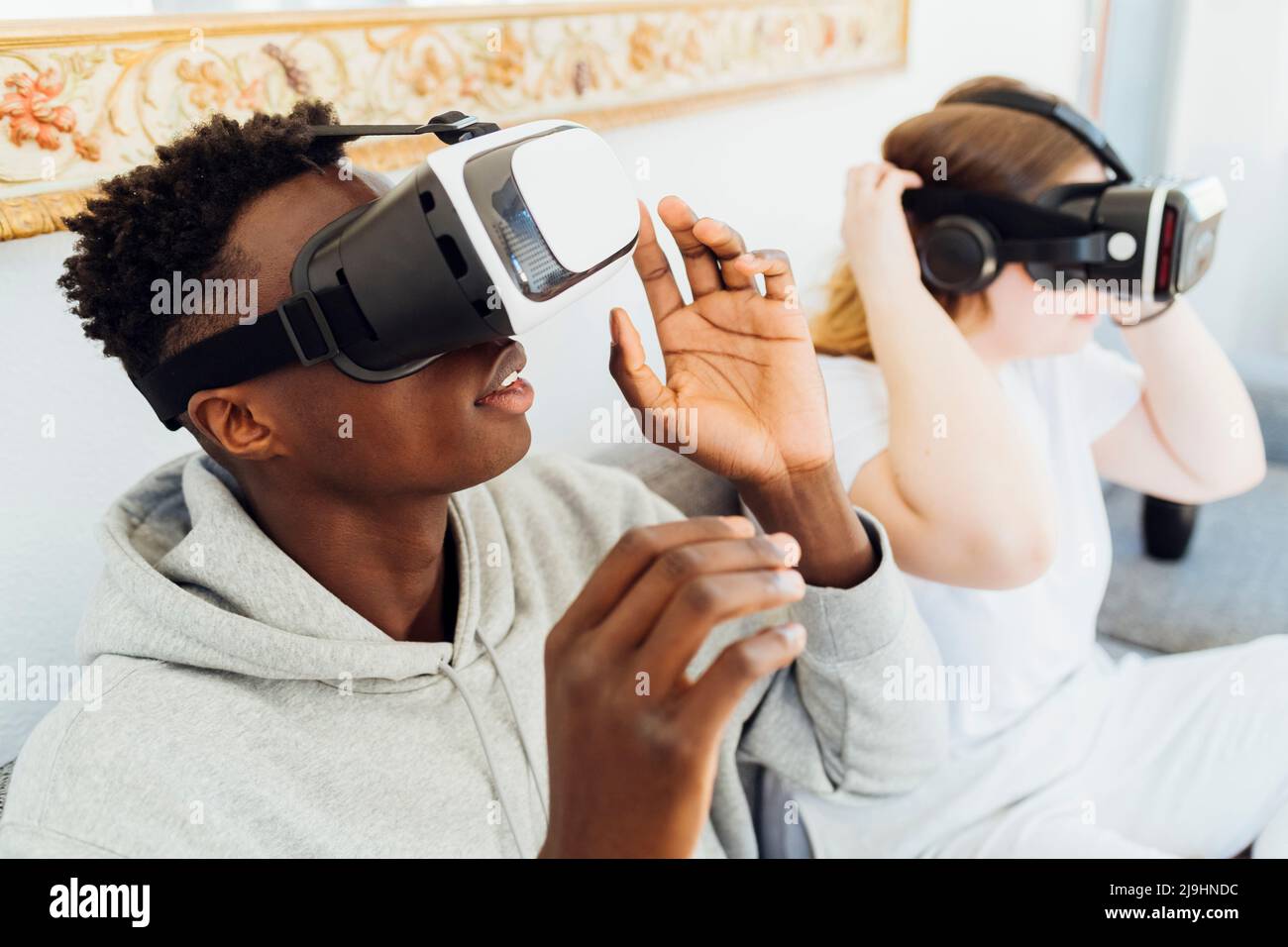 Couple wearing virtual reality simulators sitting on sofa at home Stock Photo