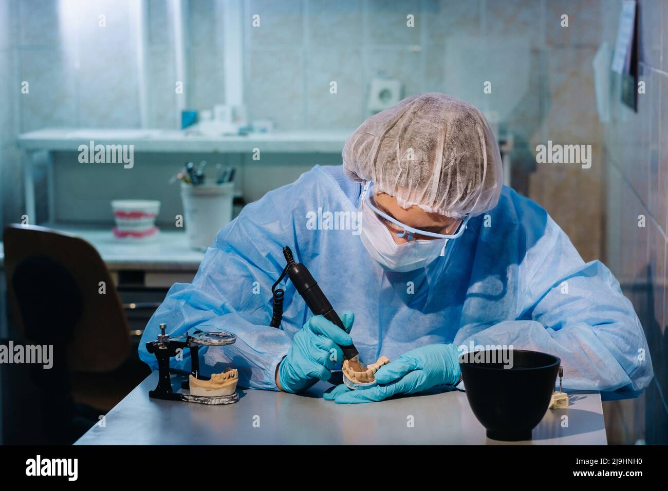 A dental technician in protective clothing is working on a prosthetic tooth in his laboratory
