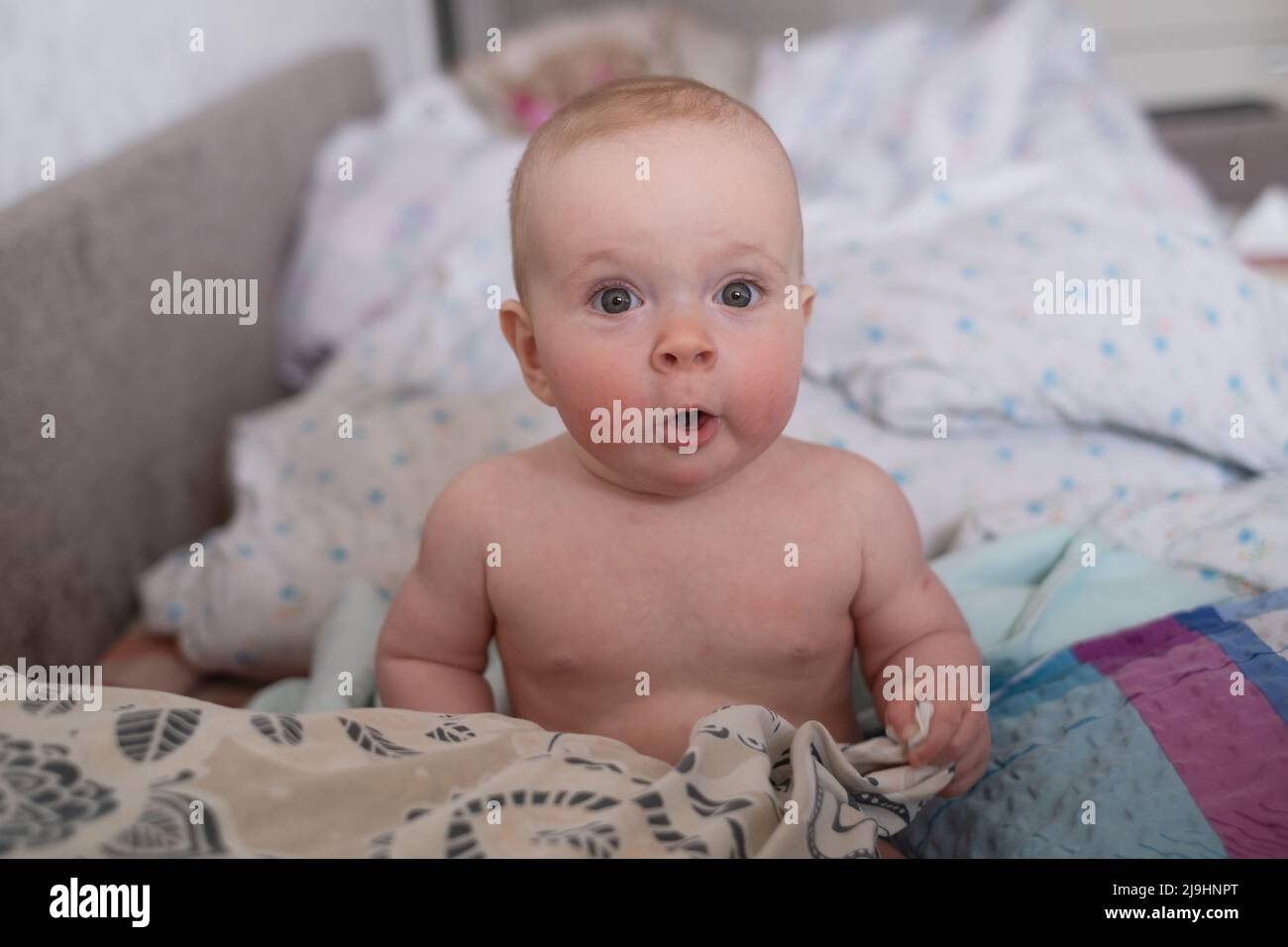 Caucasian baby in bed looking at camera with suprise. I do not want to sleep Stock Photo