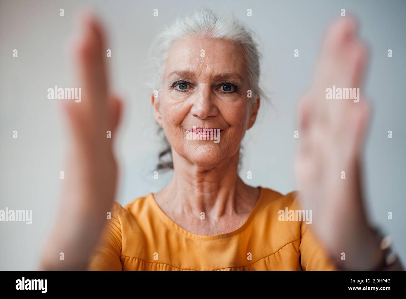 Senior woman with gray hair gesturing with hand against white background Stock Photo
