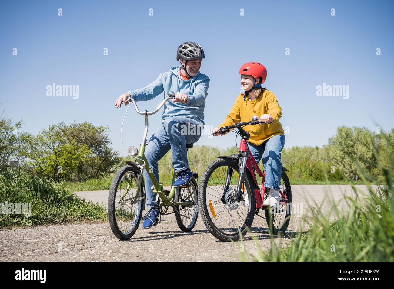Happy grandfather with granddaughter cycling on footpath Stock Photo