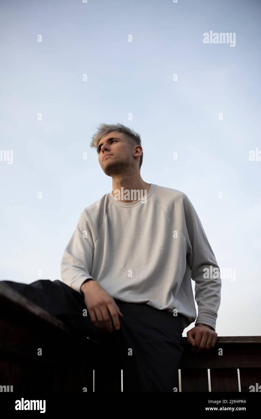 Thoughtful young man sitting on railing Stock Photo
