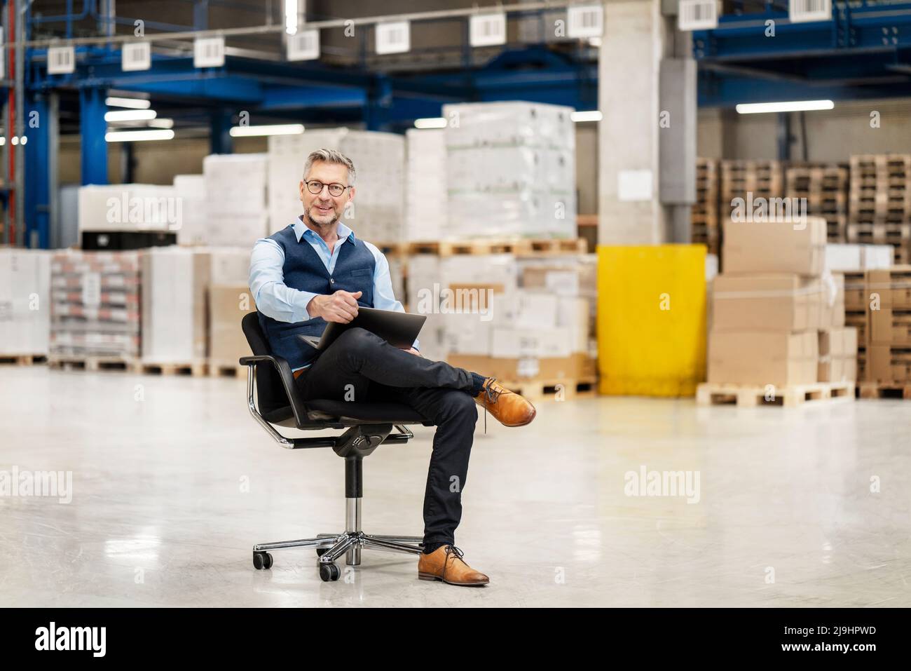 Businessman with legs crossed at knee and laptop in factory Stock Photo