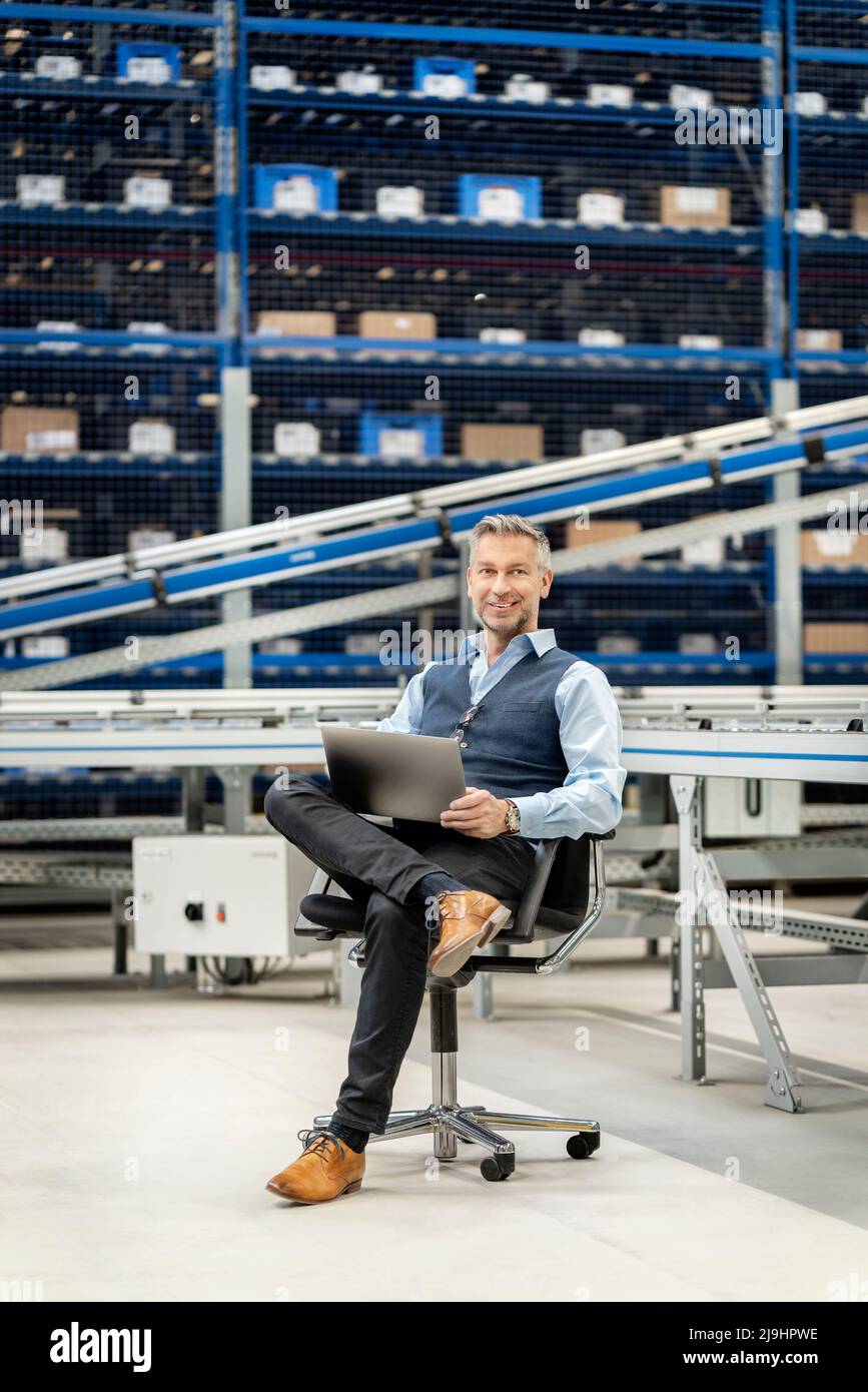 Mature businessman with legs crossed at knee in warehouse Stock Photo