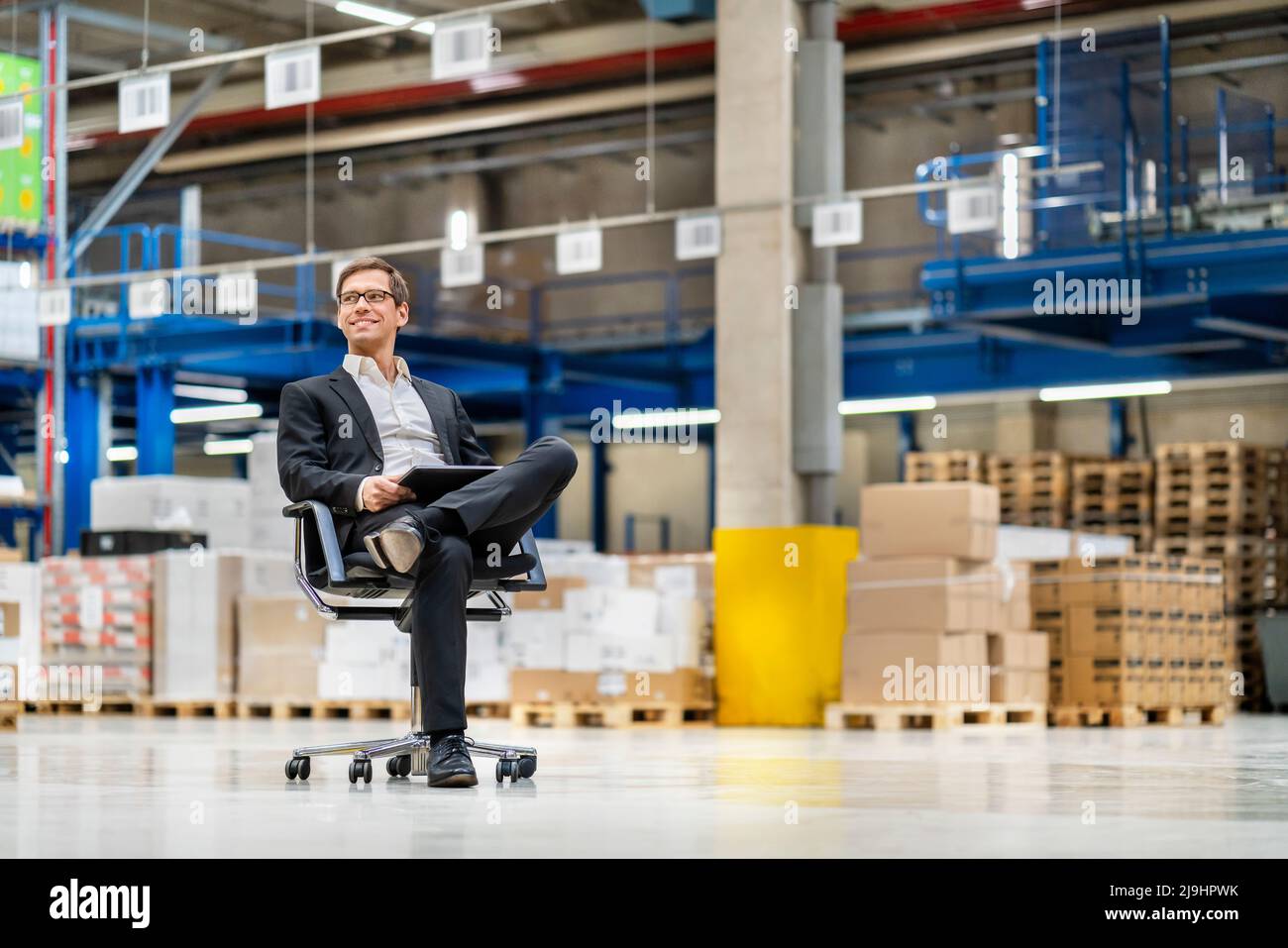 Thoughtful businessman with leg crossed at knee in warehouse Stock Photo