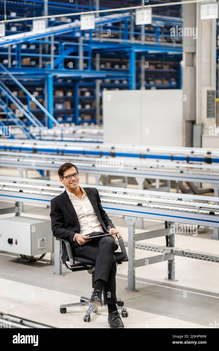 Mature businessman with legs crossed at knee in factory Stock Photo