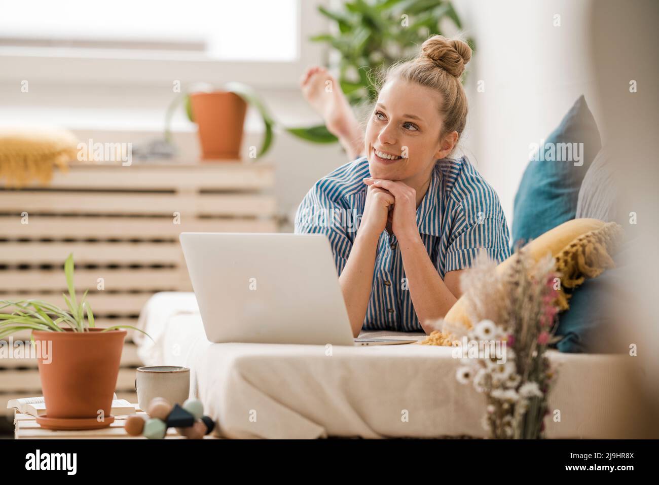 Freelancer with hand on chin day dreaming lying on bed at home Stock Photo