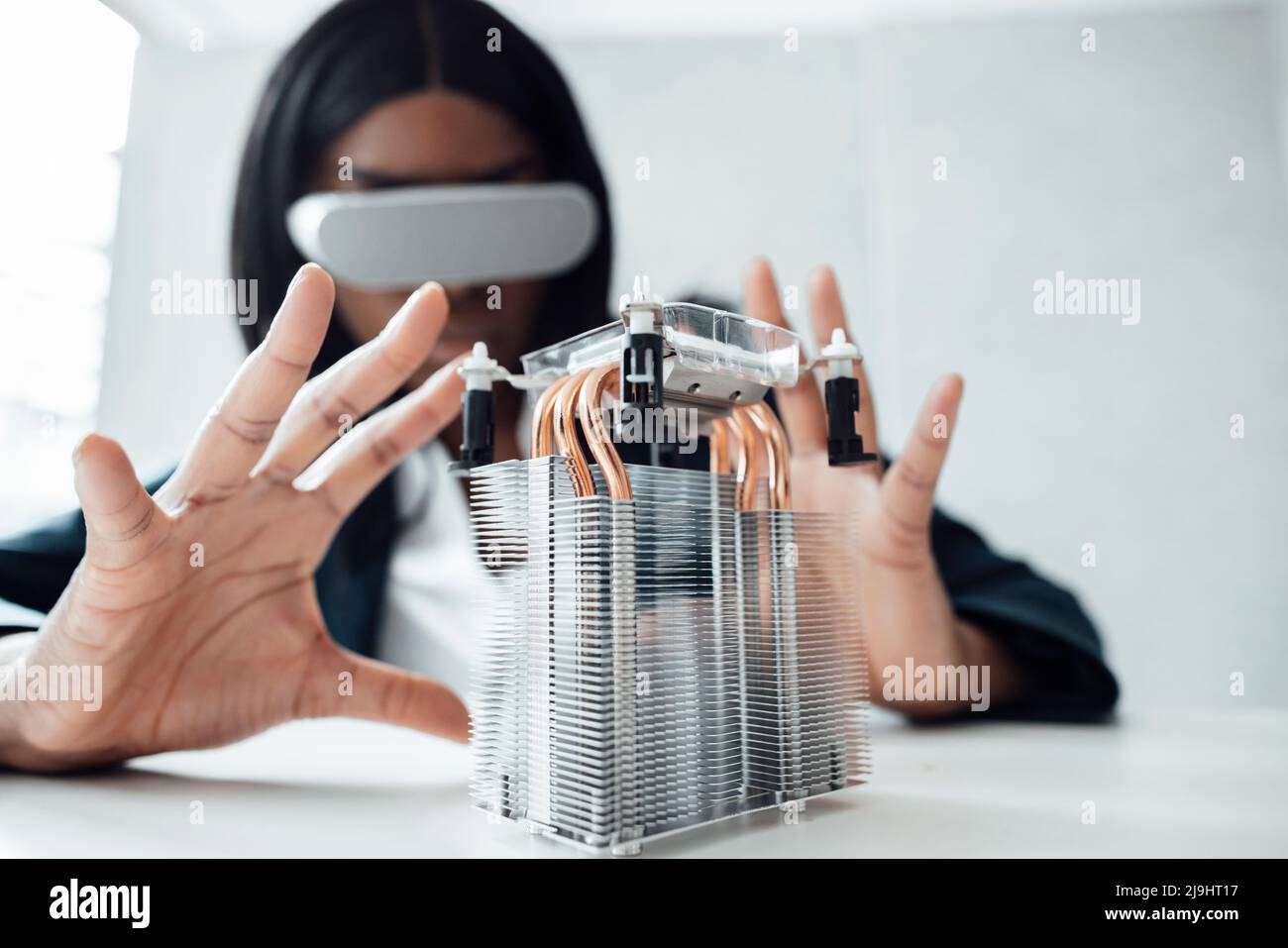Engineer wearing virtual reality simulator gesturing at machine part on desk Stock Photo