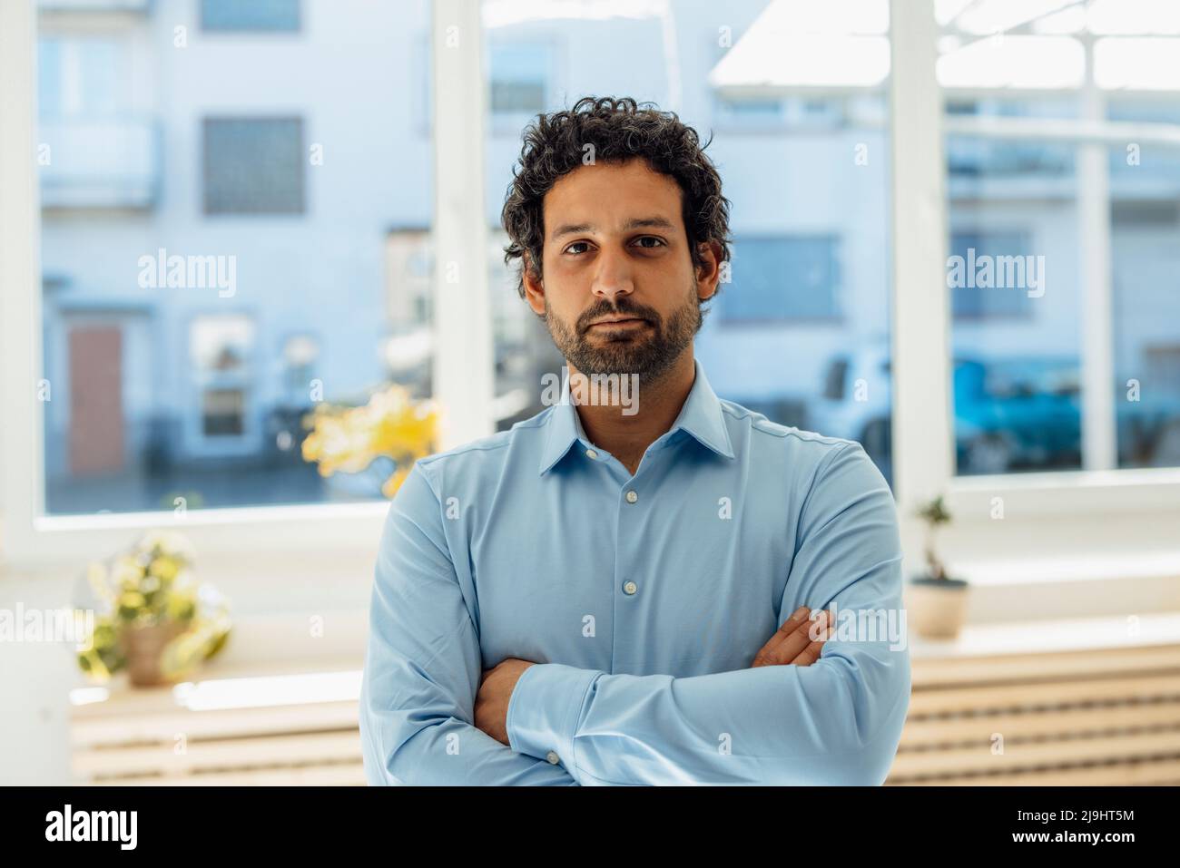 Businessman standing with arms crossed in front of window Stock Photo ...