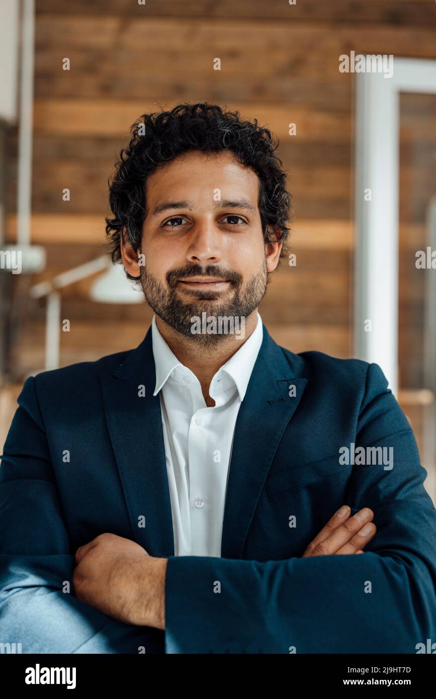 Smiling businessman standing with arms crossed in front of wall at ...