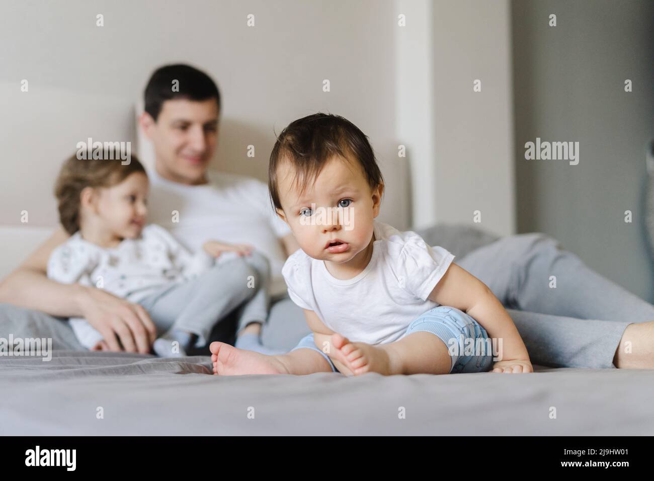 Cute baby boy with father and sister in background on bed at home Stock