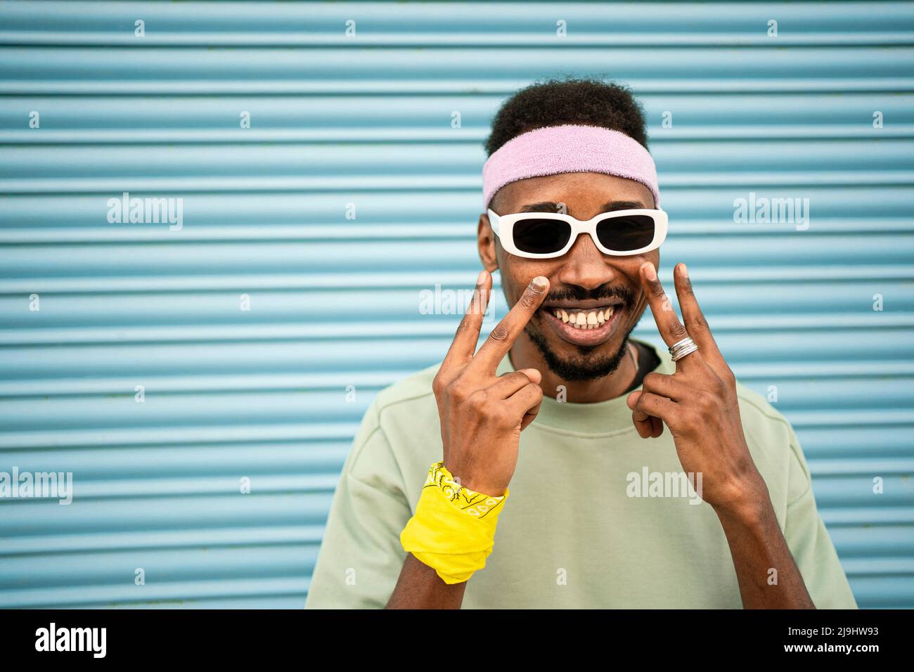 Happy man gesturing peace sign in front of blue shutter Stock Photo