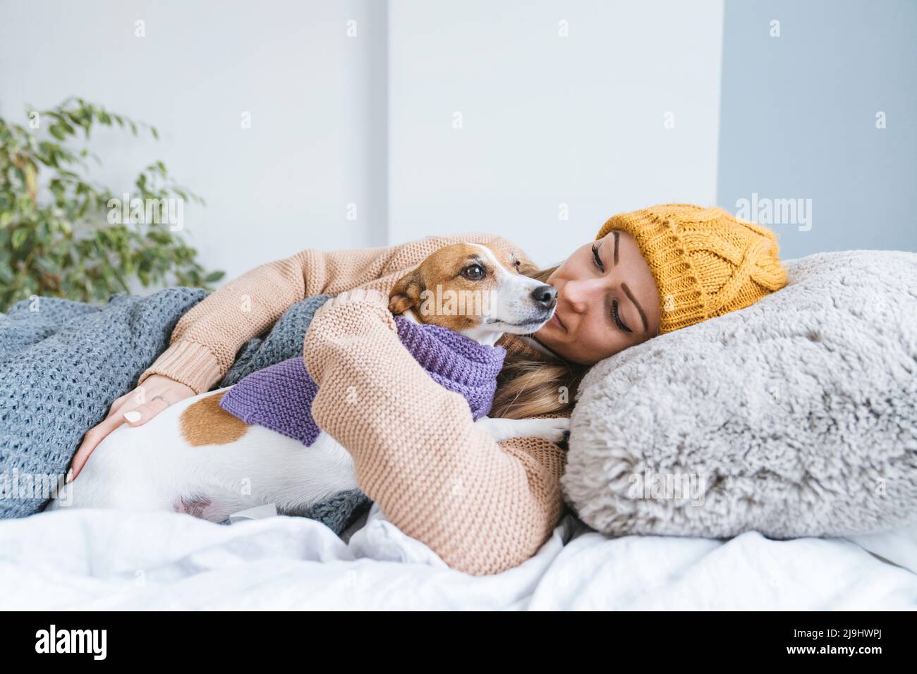 Woman wearing warm clothing cuddling with dog in bed Stock Photo Alamy