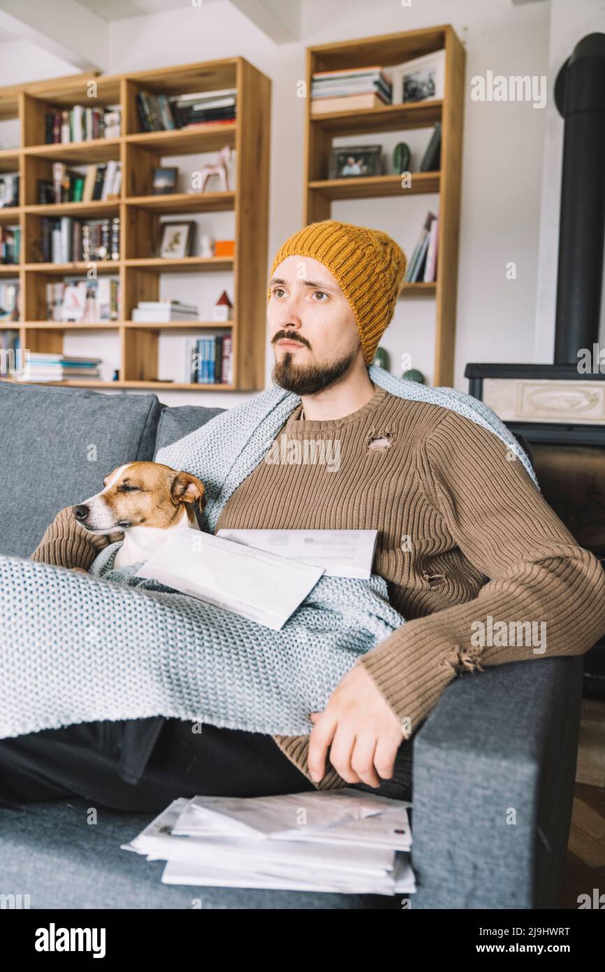 Wickede, NRW, Deutschland. Ein junger nachdenklicher Mann mit einem Jack Russell Terrier sitz auf der Sofa mit mehrere Rechnungen in den Händen Stock Photo