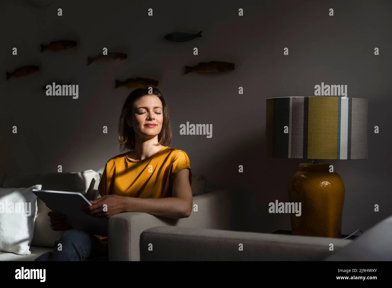 Smiling woman with tablet PC sitting on sofa in living room Stock Photo ...