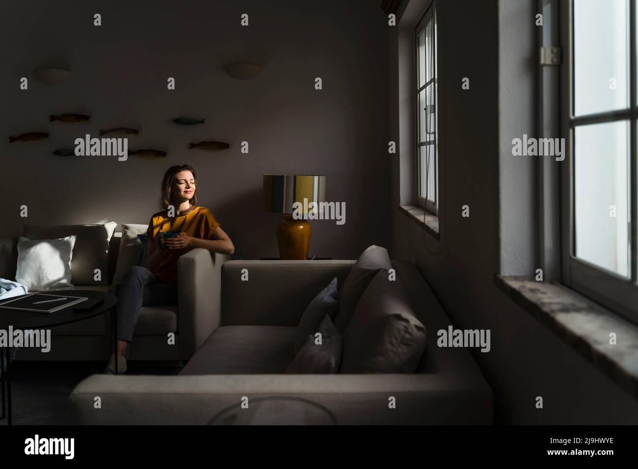 Woman with eyes closed sitting on sofa in dark living room Stock Photo ...
