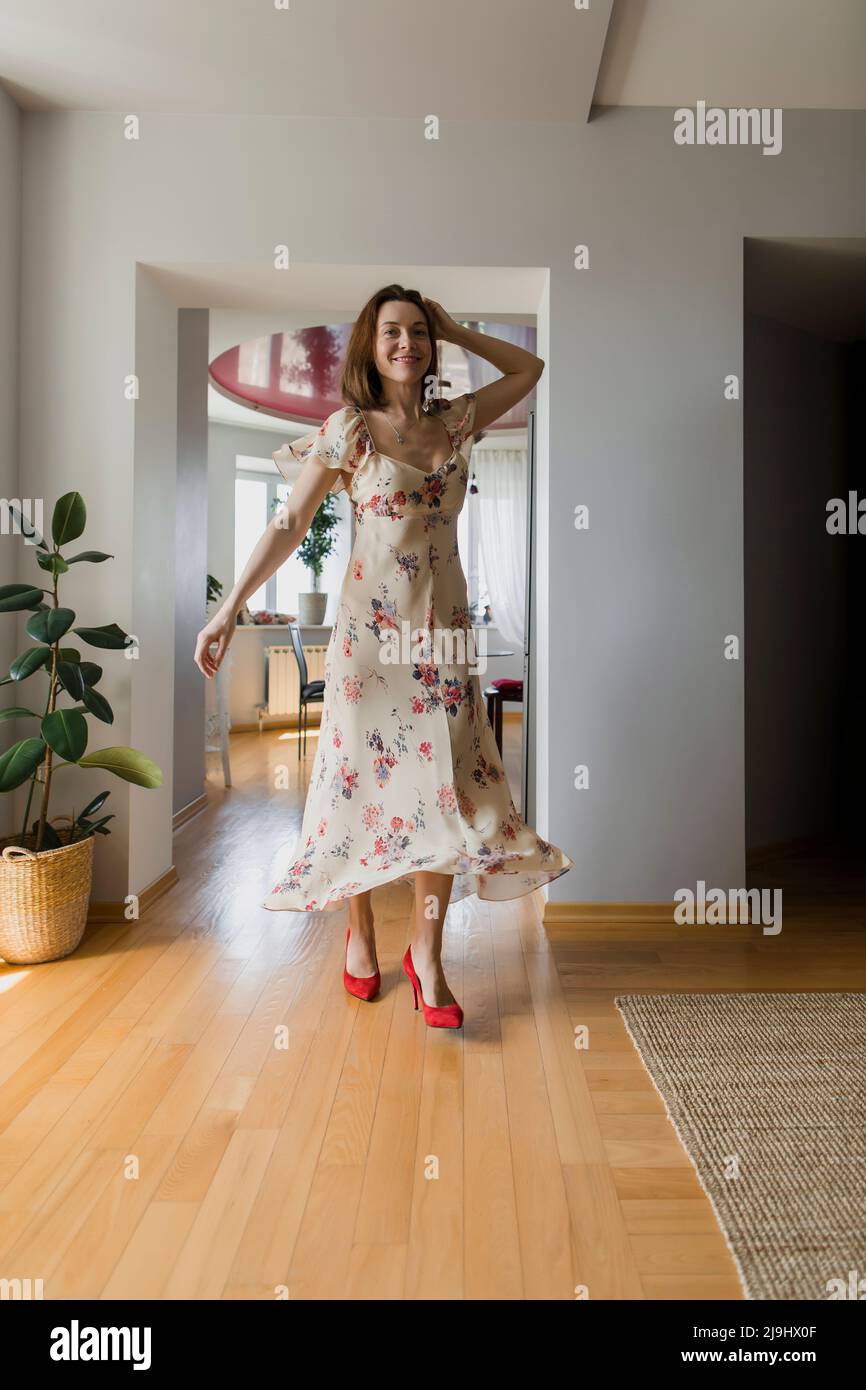 Happy woman wearing floral dress standing at home Stock Photo