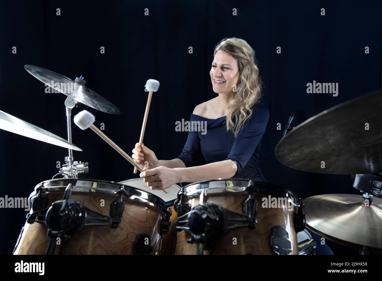 Smiling mature woman playing drums against black background Stock Photo