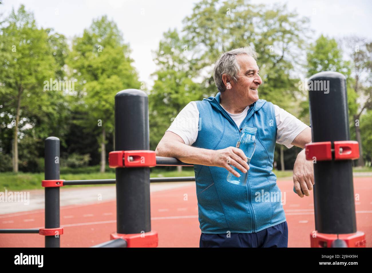 Happy senior man with water bottle standing by gymnastics bar Stock ...