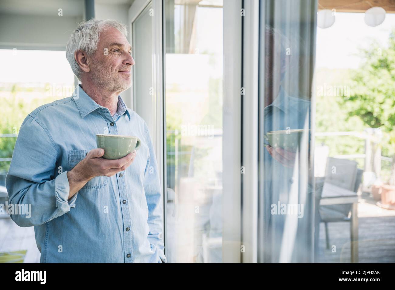 Happy senior man holding coffee cup looking out through window Stock Photo