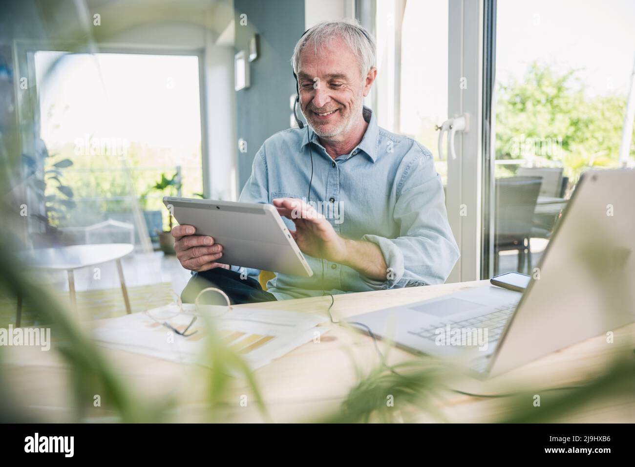 Smiling freelancer wearing headset using tablet PC at home Stock Photo