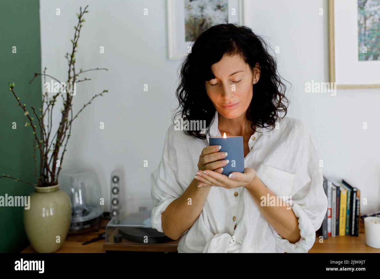 Woman with eyes closed holding candle in living room at home Stock Photo