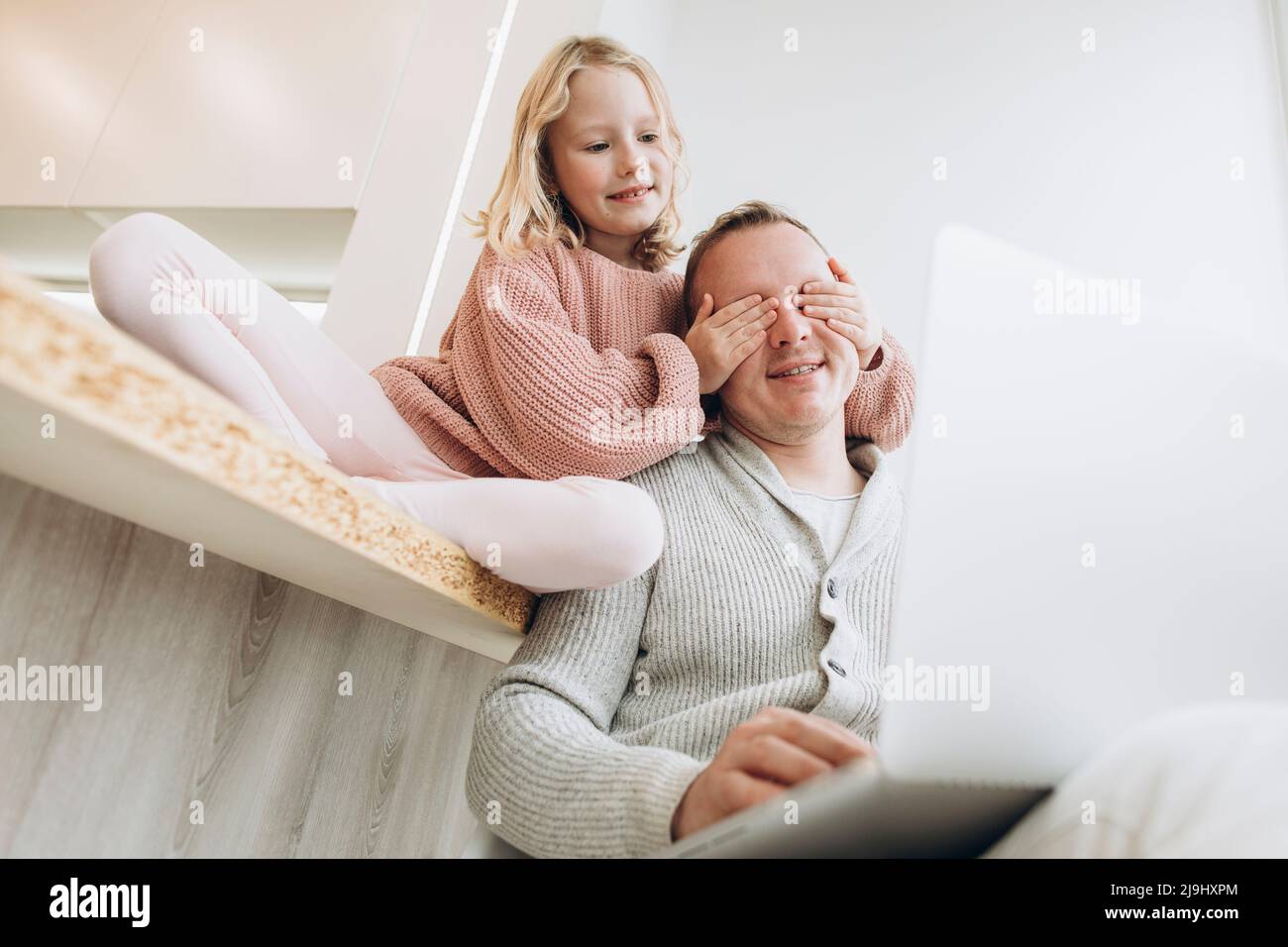 Daughter covering eyes of father sitting with laptop at home Stock Photo