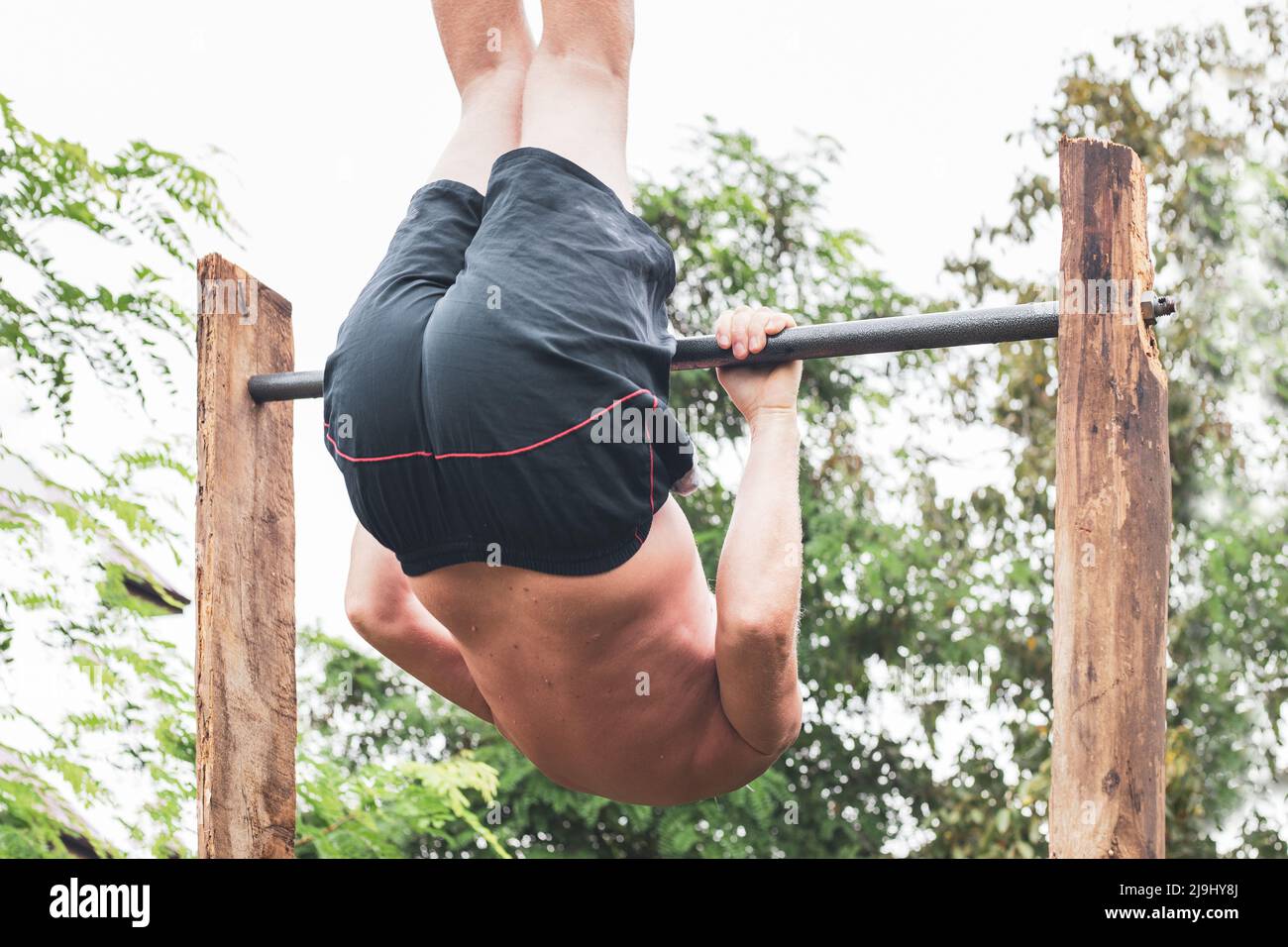 A mature man goes in for sports on a horizontal bar, somersaults and hangs upside down. Active lifestyle in retirement. Stock Photo