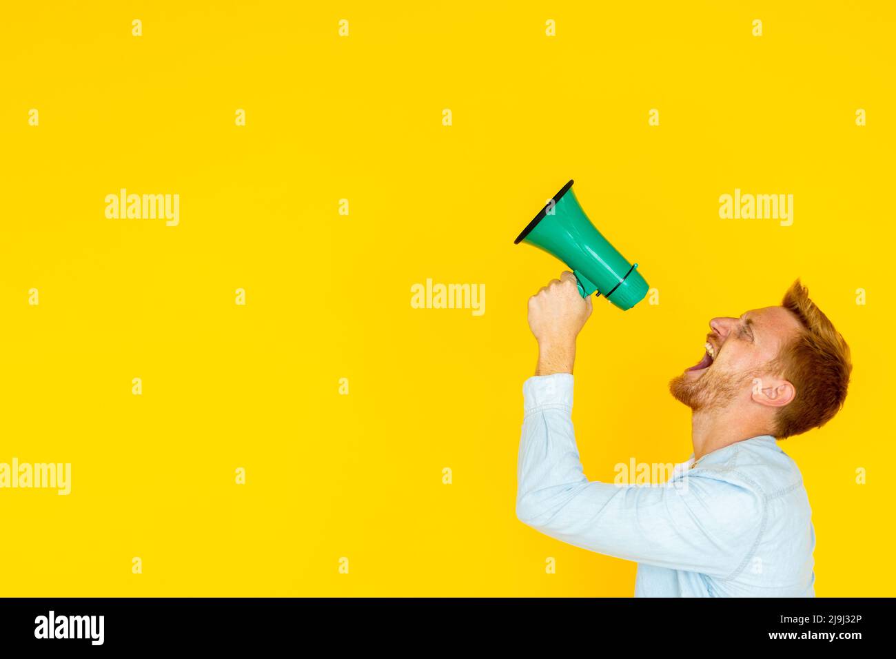 Hipster trendy man screaming through megaphone over yellow background Stock Photo