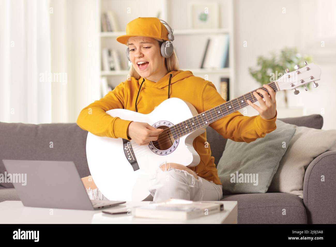 Young female playing an acoustic guitar and singing in front of a laptop computer at home Stock Photo