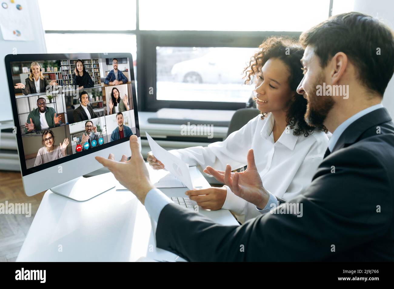 Business colleagues, co-founders of the company, sit at a table in the modern office in front of a computer screen, hold an online video conference with international colleagues, brainstorming Stock Photo