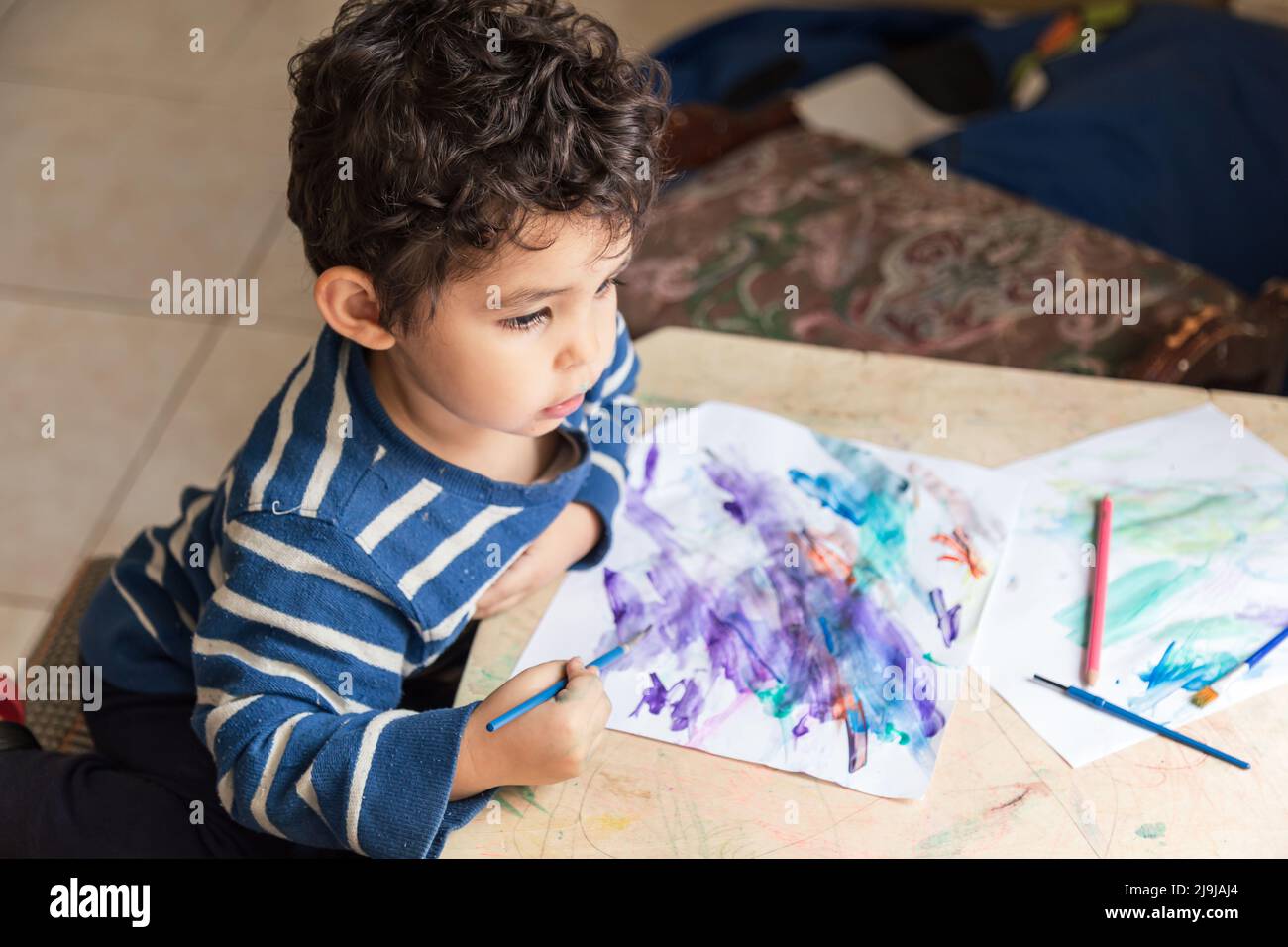 child painting with paints and colored pencil making a drawing Stock