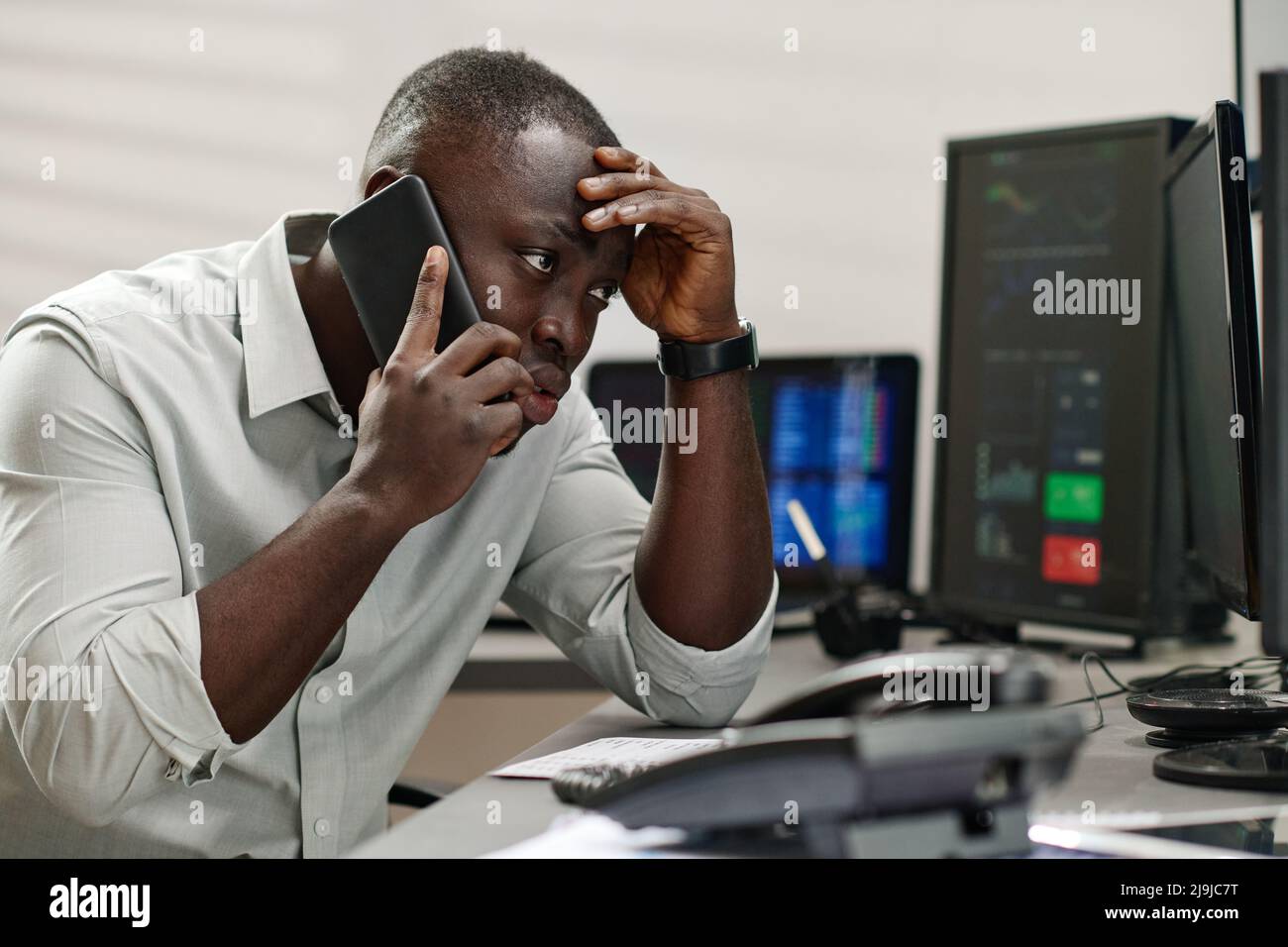 Young Black man working with in stock trading industry feeling stressed out talking to dissatisfied client Stock Photo