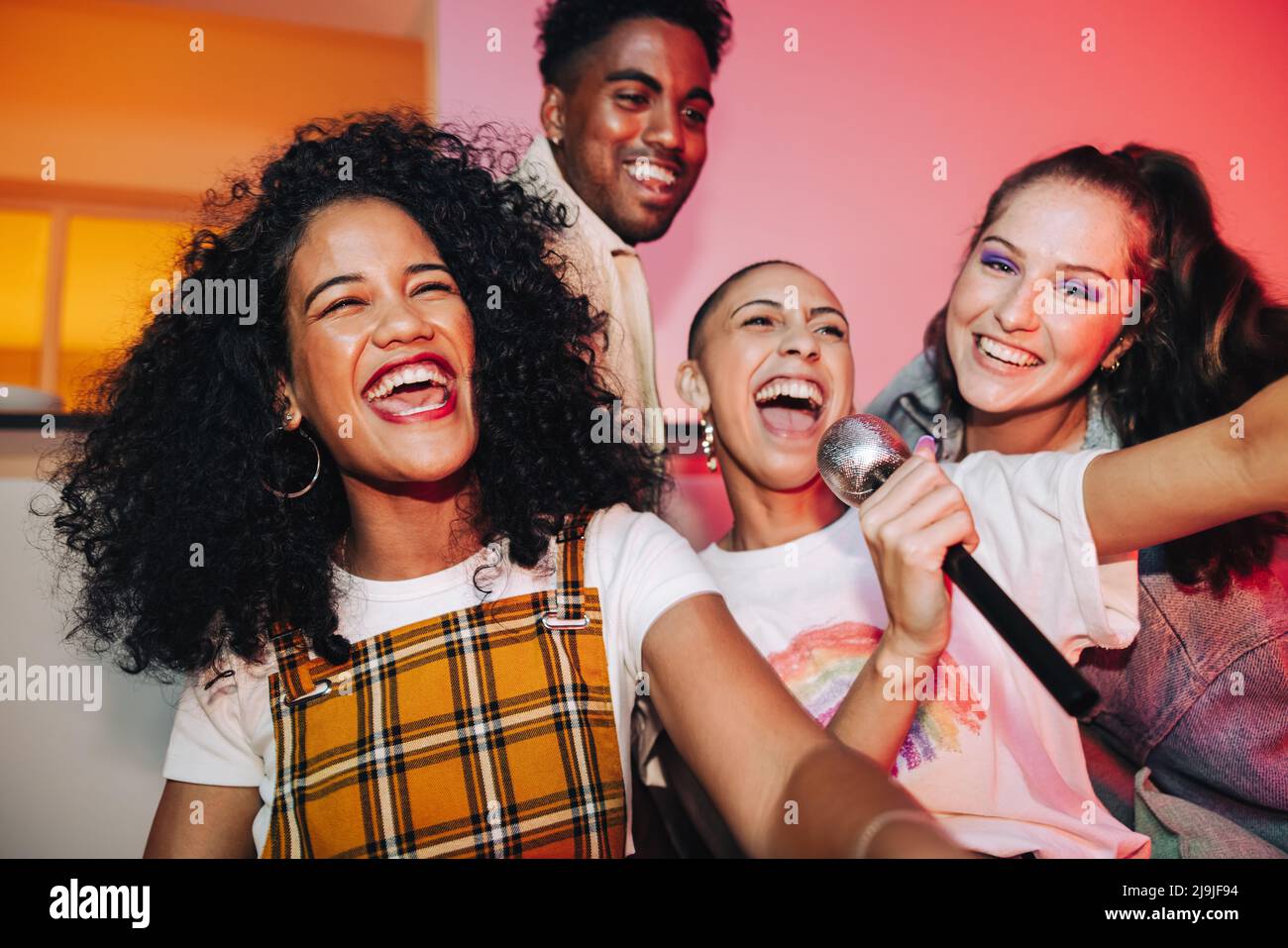 Young friends singing their favourite song during karaoke night. Happy friends laughing joyfully at a house party. Group of multicultural friends havi Stock Photo