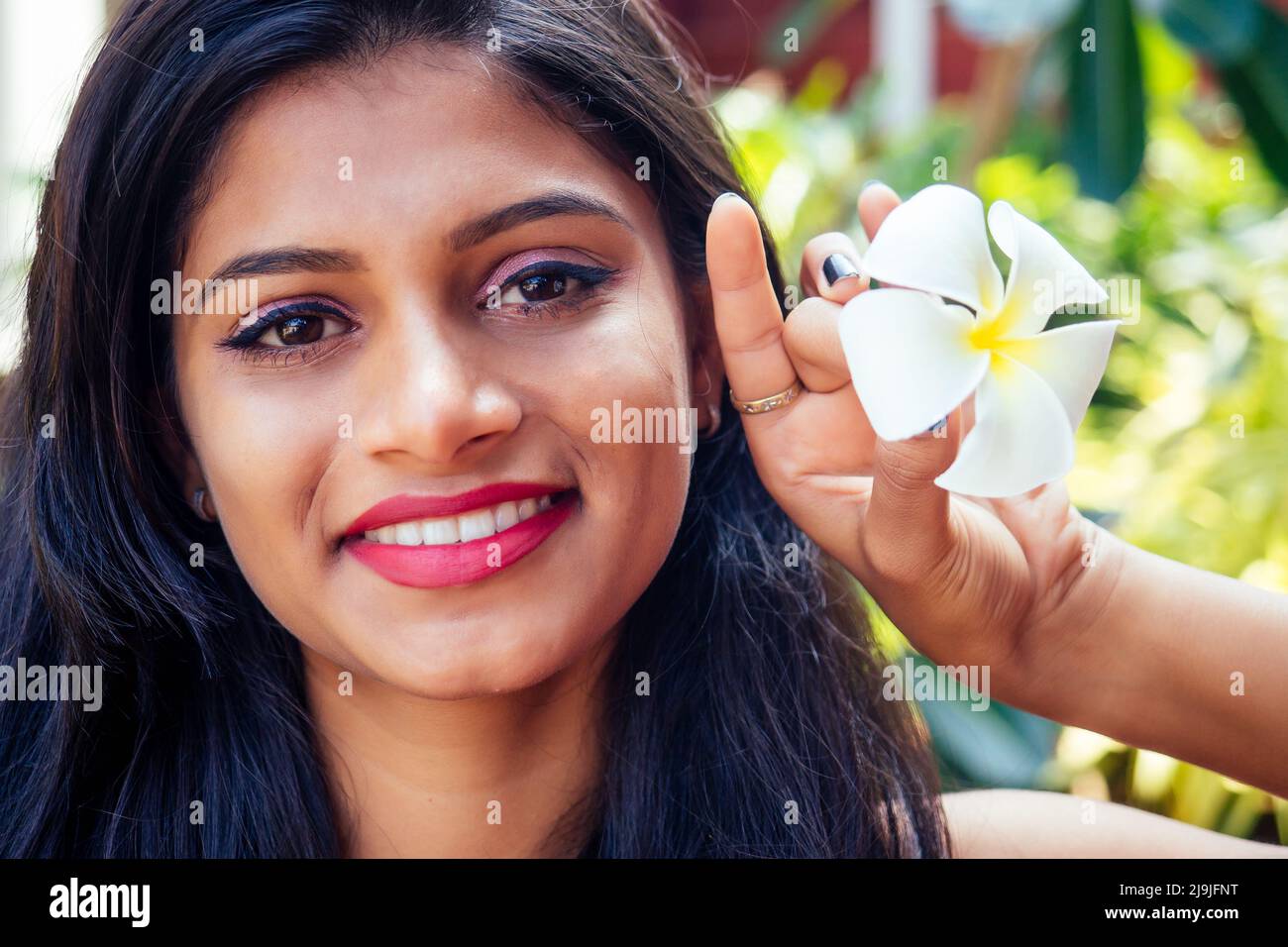 Closeup headshot portrait of attitude confident smiling happy pretty young woman background of blurred trees, plumeria flowers. Positive human emotion Stock Photo