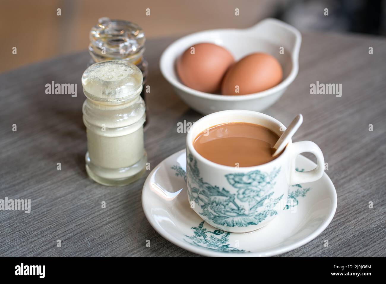 Coffee with boiled eggs, soy sauce and white pepper on table. Traditional oriental Chinese kopitiam style breakfast. Stock Photo