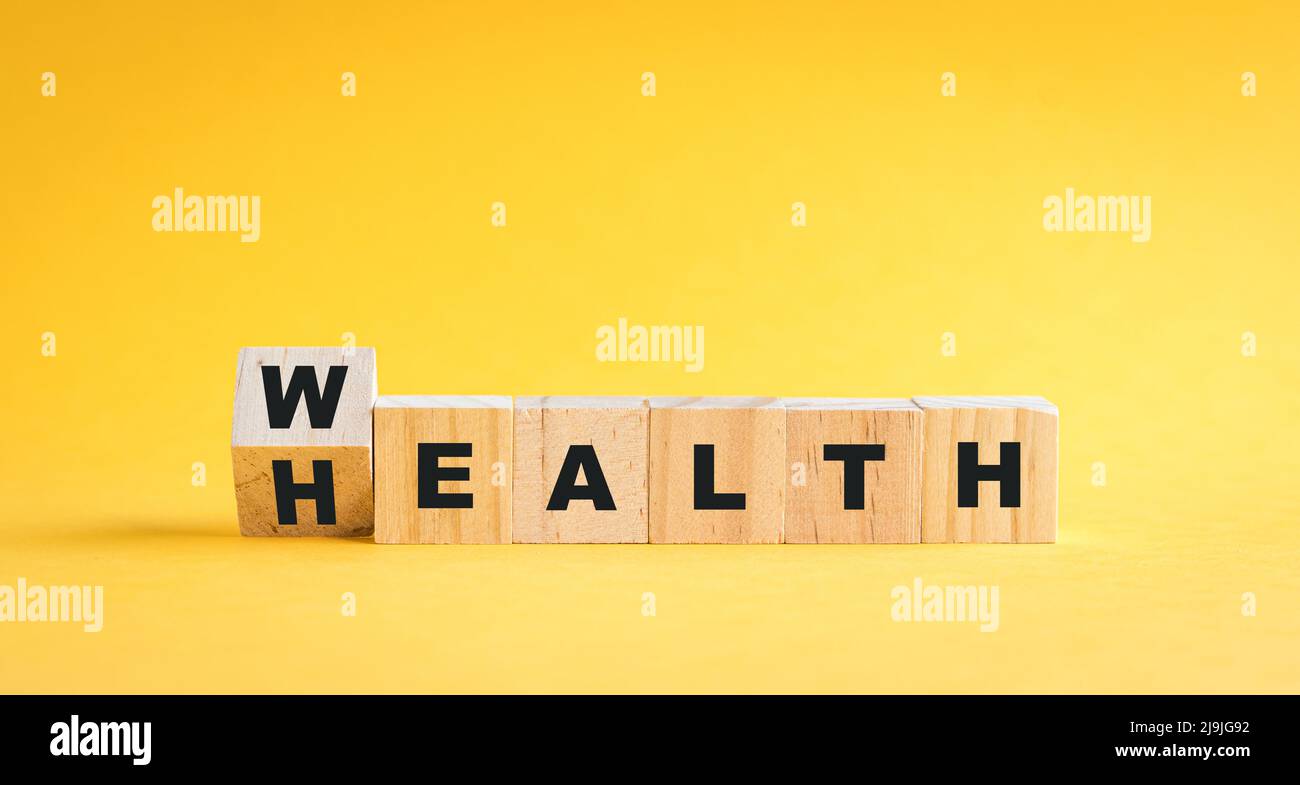 Wooden cube blocks flip from wealth to health wording. On yellow background. Stock Photo