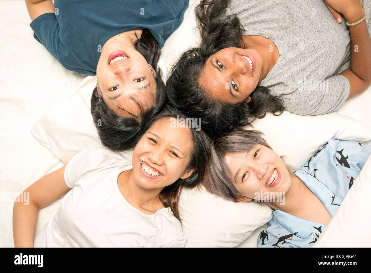Group of young multi-ethnic Asian women lying in bed, happy and smiling, top view. Friends sleep over party concept. Stock Photo