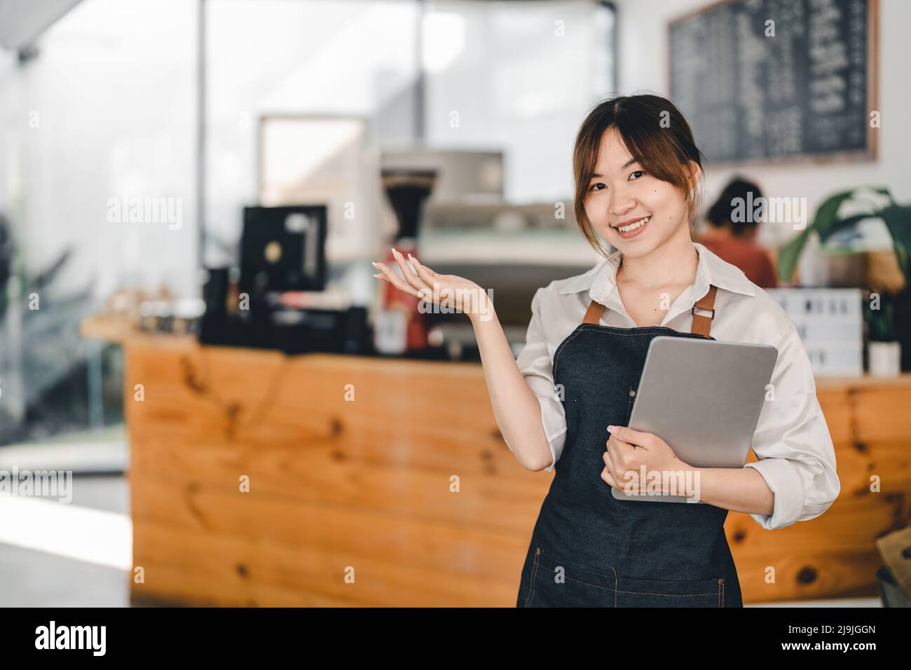 Asian woman barista holding digital tablet for checking order from customer at coffee cafe shop background , SME business concept Stock Photo