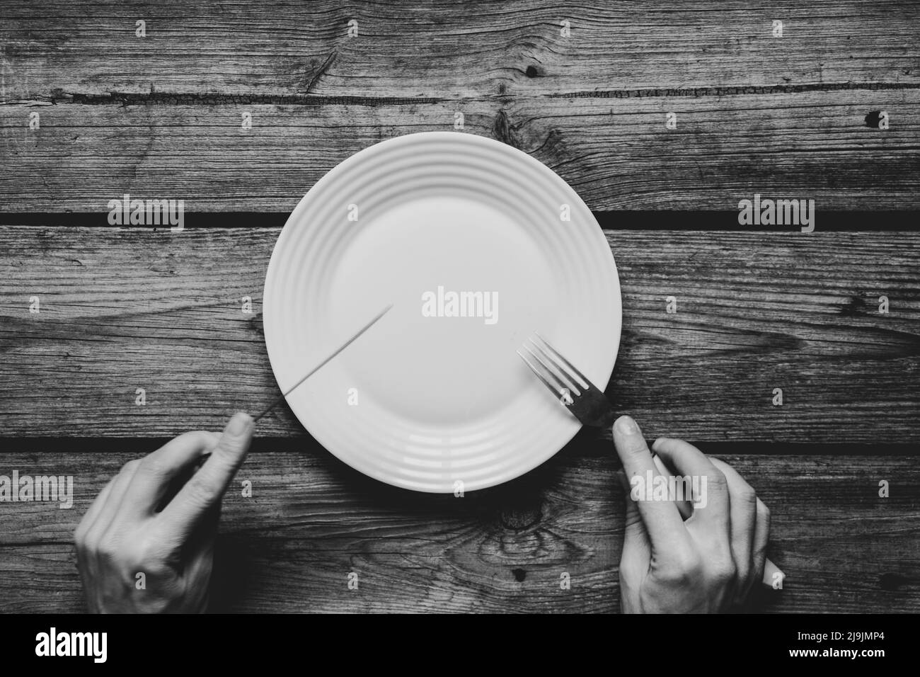 One white plate and fork with a knife in hands on an old wooden table in the kitchen at home, restaurant business, kitchen appliances Stock Photo