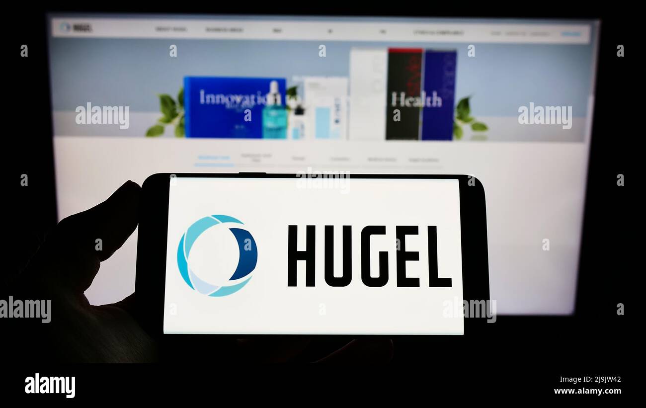 Person holding smartphone with logo of South Korean biopharmaceutical company Hugel Inc. on screen in front of website. Focus on phone display. Stock Photo