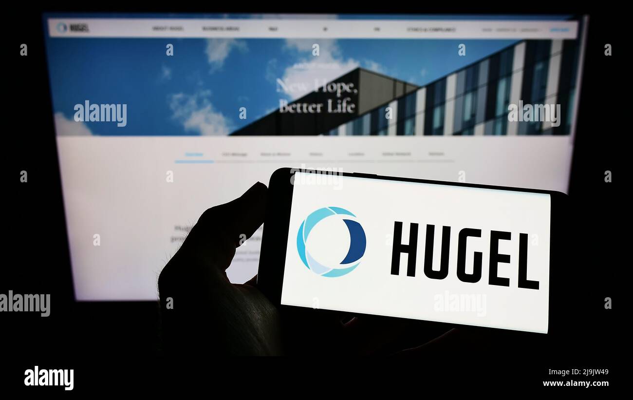 Person holding cellphone with logo of South Korean biopharmaceutical company Hugel Inc. on screen in front of webpage. Focus on phone display. Stock Photo