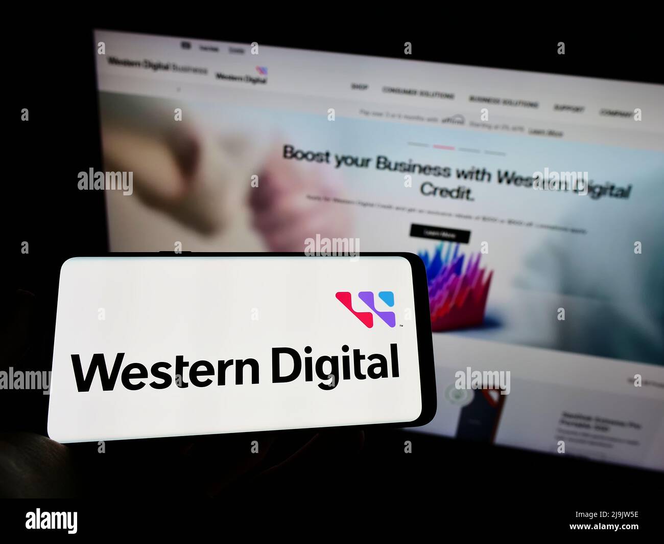 Person holding mobile phone with logo of US company Western Digital Corporation (WDC) on screen in front of web page. Focus on phone display. Stock Photo