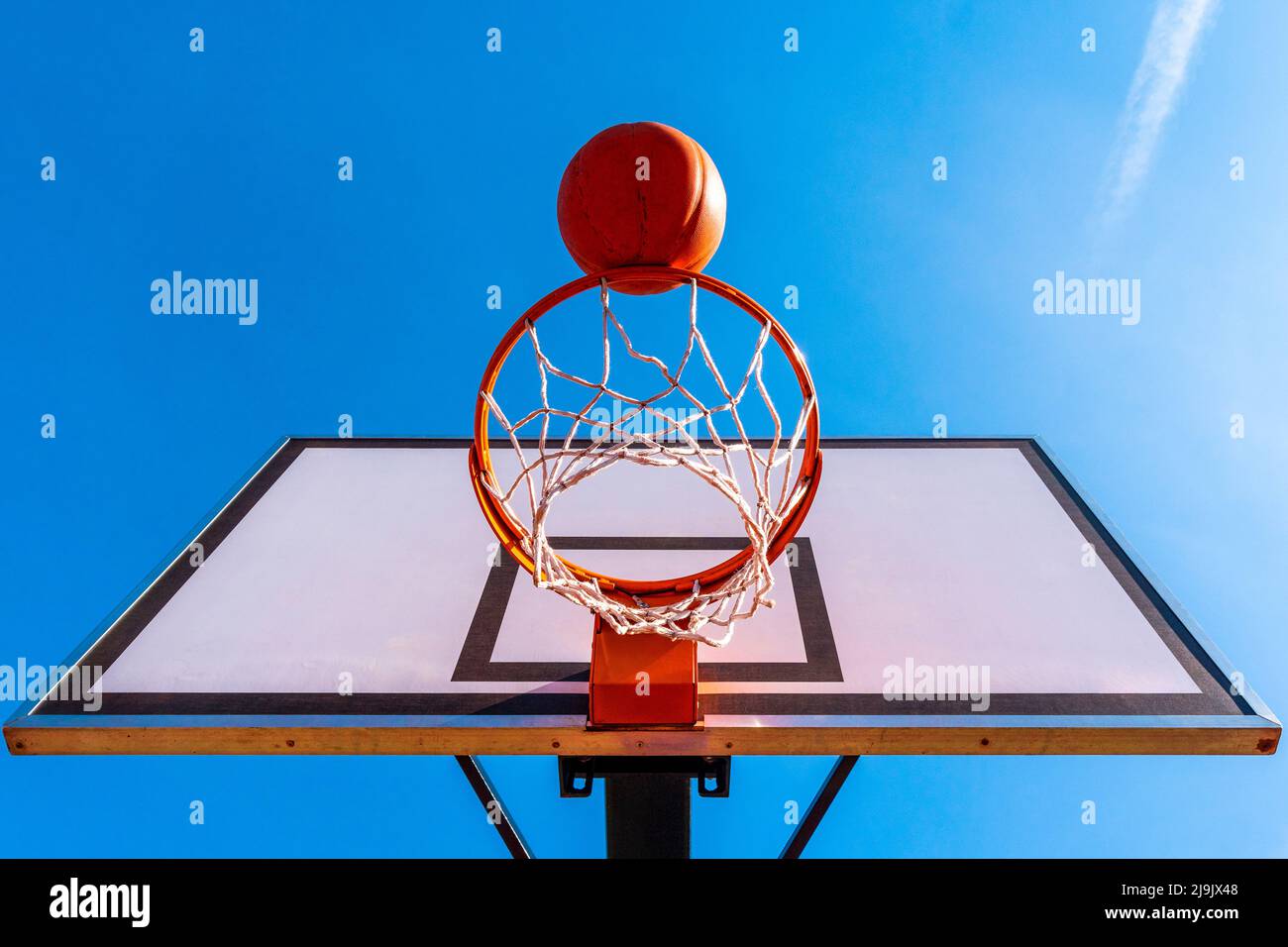 Orange basketball ball falling into the hoop. Urban youth game. Concept of success, scoring points and winning. Low angle view. Stock Photo