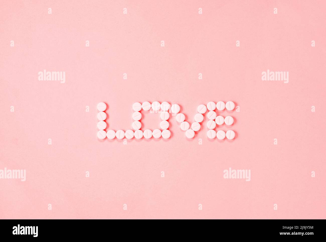 Single word LOVE made with white pills on pink background, Stock Photo