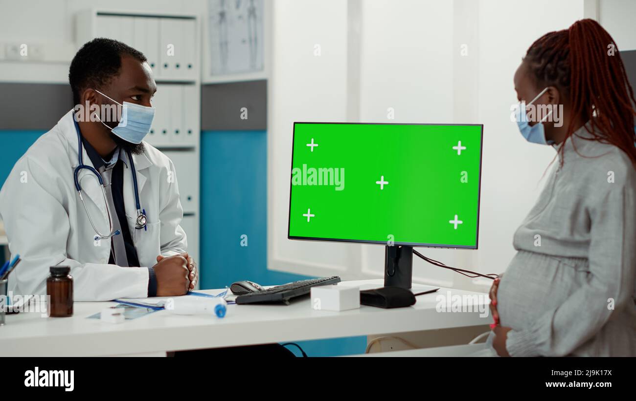 Male medic and pregnant woman with face mask looking at greenscreen on