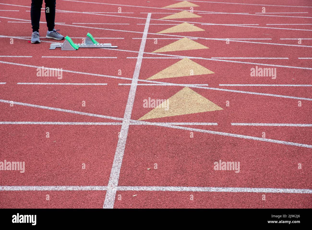One runner stands by a starting block on an empty athletic track Stock Photo