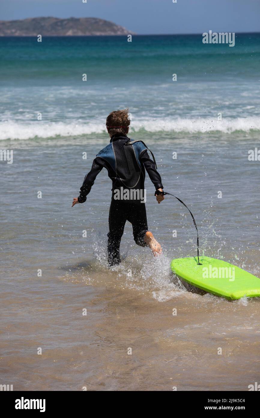 Carefree boy in wet suit running with body board in sunny ocean water Stock Photo