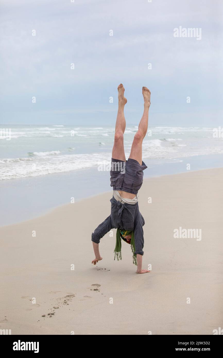 Carefree woman doing handstand on sandy ocean beach Stock Photo