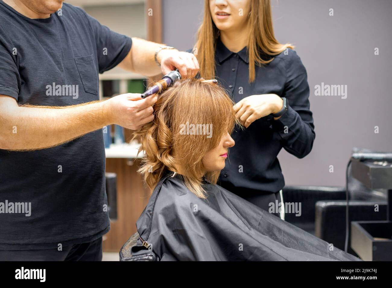 Two hairstylists make curls hairstyle of long brown hair with the